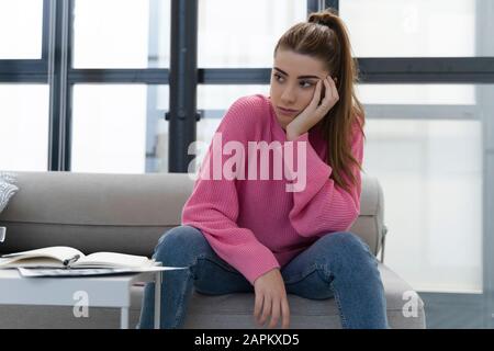 Portrait of pensive young woman sitting on the couch Stock Photo