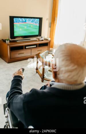 Back view of senior man watching TV at home using remote control Stock Photo