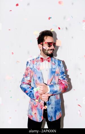 Cool and stylish man wearing a colorful suit and sunglasses smiling at a party surrounded by confetti Stock Photo