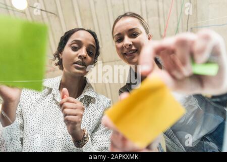 Two young businesswomen working on adhesive notes on glass table Stock Photo
