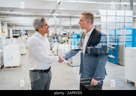 Two businessmen shaking hands in a factory Stock Photo