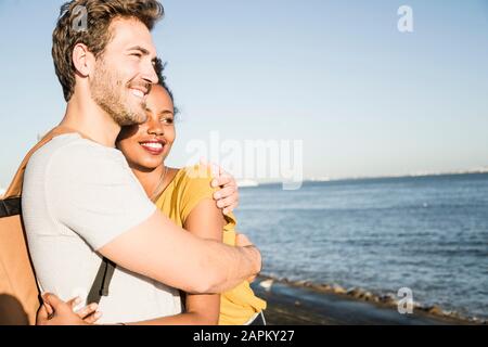 Happy young couple hugging at the waterfront, Lisbon, Portugal Stock Photo