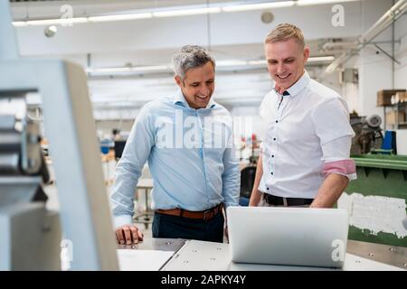 Two smiling colleagues using laptop in a factory Stock Photo