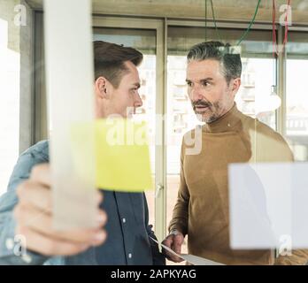 Mature businessman and young man working on adhesive notes at glass pane in office Stock Photo