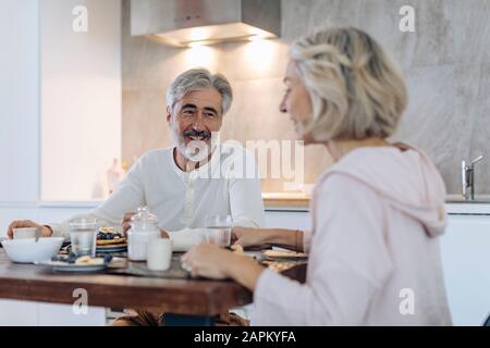 Happy mature couple sitting at table in kitchen at home having breakfast Stock Photo