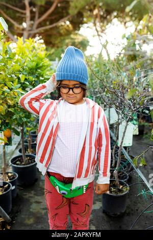 Portrait of boy at plant nursery wearing glasses and woolly hat Stock Photo