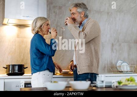Mature couple drinking red wine in kitchen at home Stock Photo