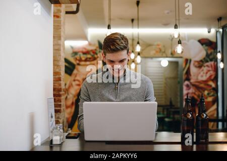 Young man sitting in a restaurant typing on his laptop while smiling Stock Photo