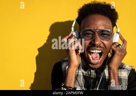 Portrait of screaming young man against yellow wall listening favourite song with headphones Stock Photo
