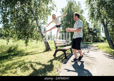 Father watching daughter balancing on a bench in park Stock Photo