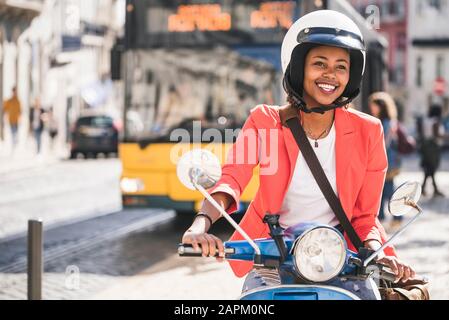 Happy young woman riding motor scooter in the city, Lisbon, Portugal Stock Photo
