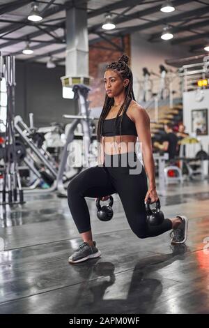 Female athlete doing lunges with kettlebells Stock Photo