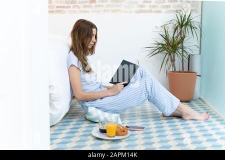 Young woman sitting on the floor and reading a book in bedroom Stock Photo