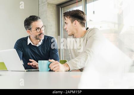 Mature businessman and young man talking at desk in office Stock Photo
