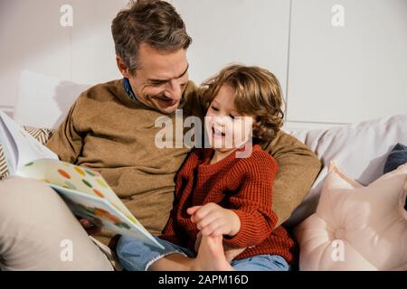 Happy father sitting with daughter on couch Stock Photo
