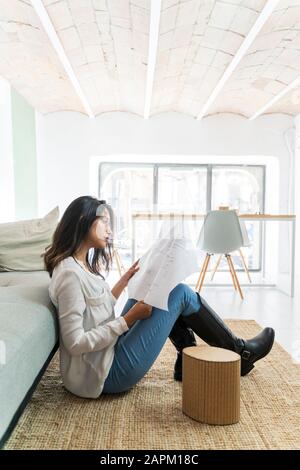 Young architect sitting on the floor of a studio looking at construction plan Stock Photo
