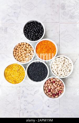 Various legumes in bowls: chickpeas, cannellini beans, quail beans, black beans, yellow lentils, red lentils, black lentils Stock Photo