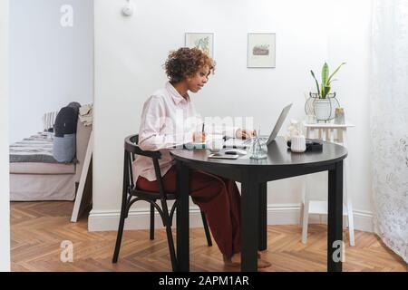 Young woman working at home taking notes and using laptop Stock Photo