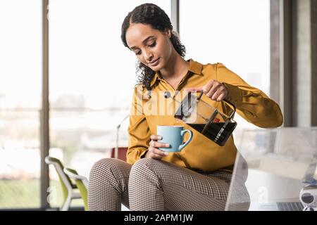 Young businesswoman sitting on desk in office having a coffee break Stock Photo