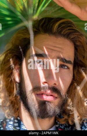 Portrait of bearded young man with dyed hair under palm leaf Stock Photo