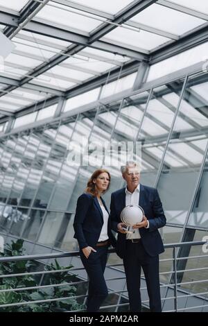 Businessman and businesswoman holding globe in modern office building Stock Photo