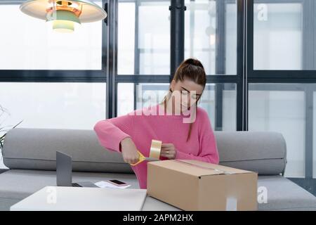 Young woman sitting on couch packing parcel Stock Photo