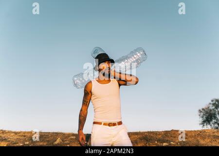 Young man holding empty plastic bottles in barren land Stock Photo