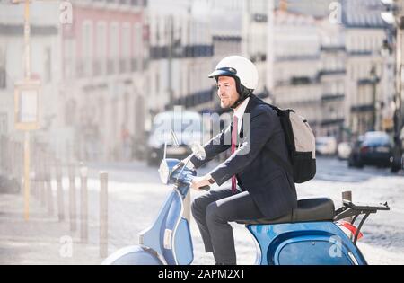 Young businessman riding motor scooter in the city, Lisbon, Portugal Stock Photo