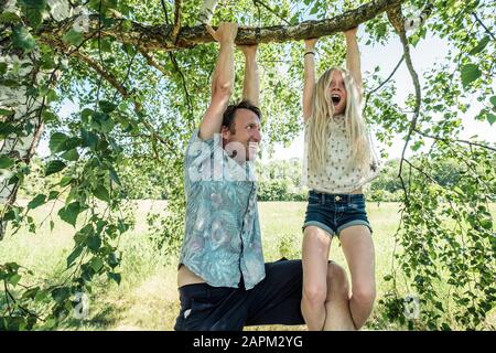 Father and daughter hanging on a branch of a birch tree Stock Photo
