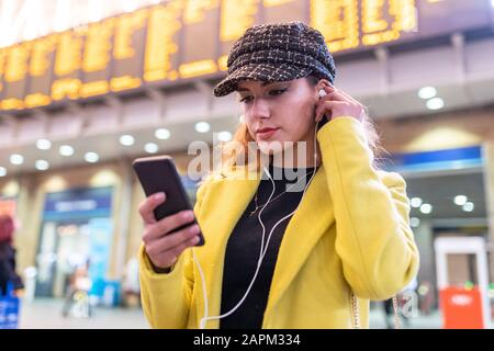 Woman at train station checking her smartphone and using earphones Stock Photo