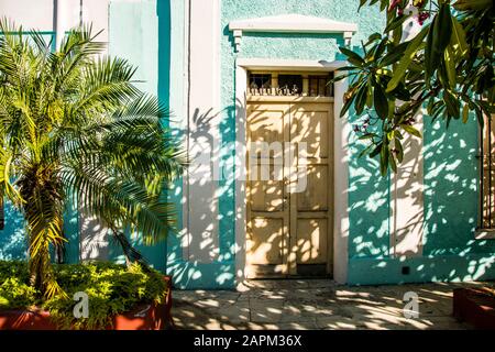 A home painted turquoise, with a yellow door, surrounding by palm trees; Santiago de Cuba, Cuba. Stock Photo
