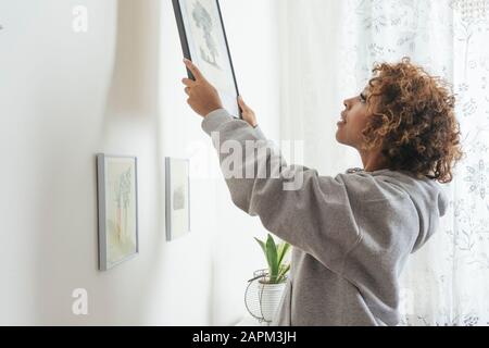 Young woman hanging up picture at home Stock Photo