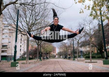 Portrait of young woman in black sportswear jumping in the air while listening music with headphones Stock Photo