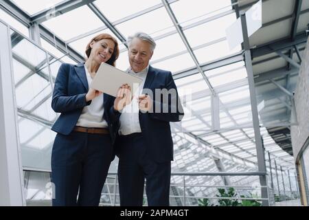 Smiling businessman and businesswoman using tablet in modern office building Stock Photo