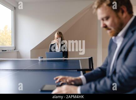 Businessman and businesswoman working at table tennis table in office Stock Photo