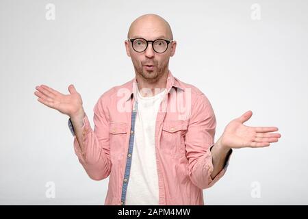 Can not be. Surprised bald man with glasses, spreads hand to the sides and looks into the camera with big eyes. Stock Photo