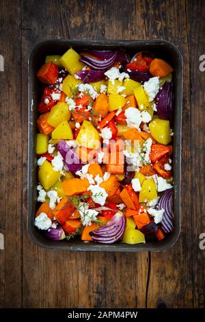 Chopped vegetables: hokkaido pumpkin, potatoes, bell pepper and red onions with thyme and feta cheese on baking tray Stock Photo