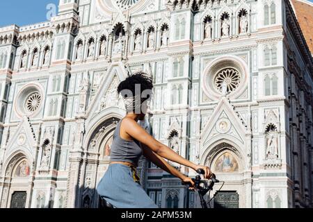 Young woman riding bicycle in front of cathedral, Florence, Italy Stock Photo