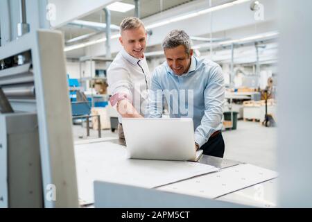 Two smiling colleagues using laptop in a factory Stock Photo