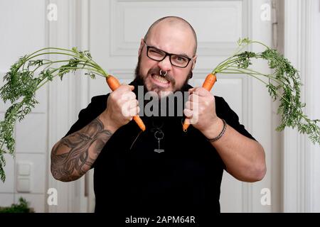 Portrait of angry bearded man holding carrots in kitchen Stock Photo