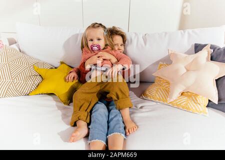 Two little sisters cuddling on couch at home Stock Photo