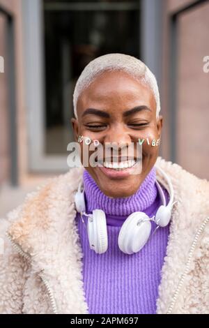 Portrait of mature white haired woman with white headphones and stickers in her face, good vibes Stock Photo