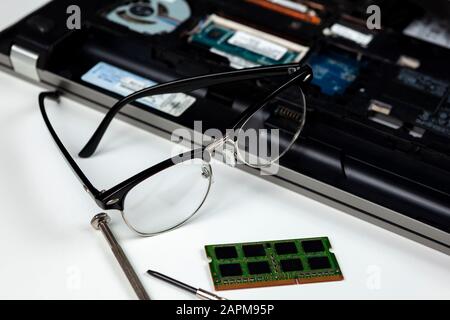 IT engineers spectacles laying on a laptop he is repairing and upgrading the memory to Stock Photo