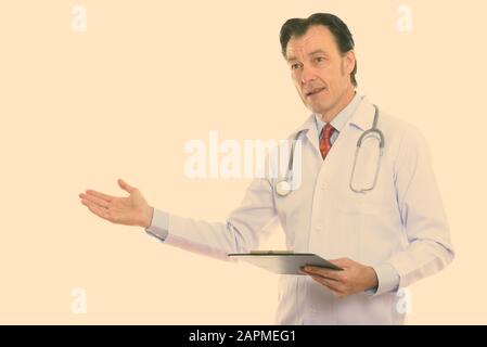 Studio shot of mature handsome man doctor holding clipboard and showing something Stock Photo