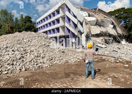 Engineer holding tablet is checking for destruction, demolishing building. Stock Photo