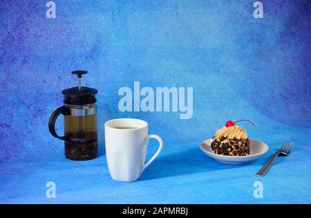 Sweet breakfast, tea cup plate with sponge cake in chocolate chips with cherries and tea teapot on a blue abstract background. Close-up. Stock Photo