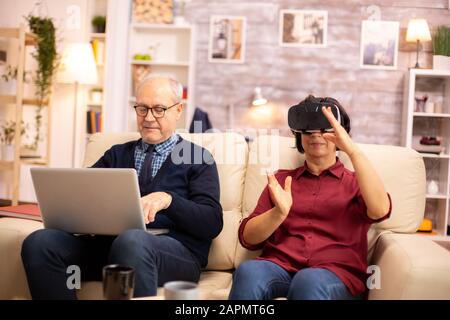 Old elderly retired woman in her 60s experiencing virtual reality for the first time in their cozy apartment Stock Photo