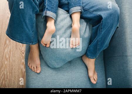 Adult woman feet and child heels top view. Mother and daughter lying on couch and hugging. Home concept. Stock Photo