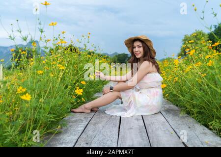 happy woman sitting on wooden bridge with yellow cosmos flower field Stock Photo