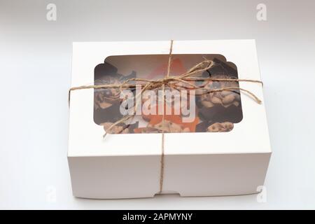 box tied with a rope with a transparent lid with chocolate cupcakes with cream top and crispy topping in paper on a white background Stock Photo